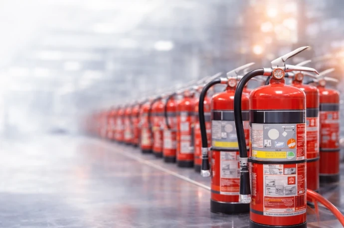 Fila de extintores de incendios rojos alineados en suelo industrial con fondo desenfocado, instalación profesional de protección contra incendios.